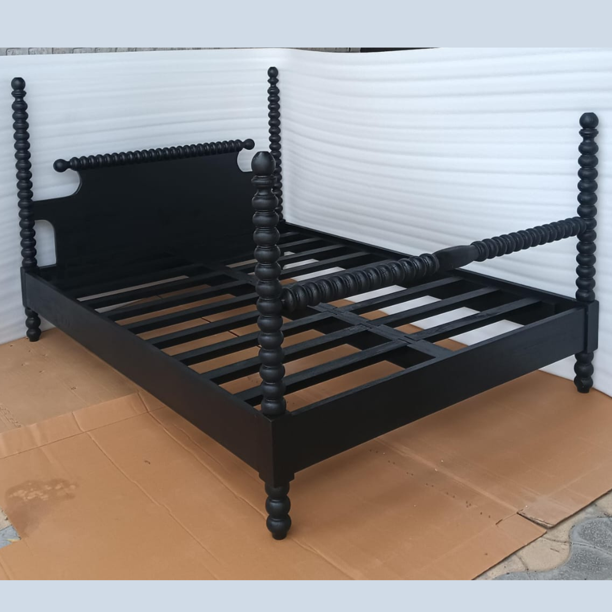 Angled view of handmade black wooden four-poster bed showing carved posts and support slats